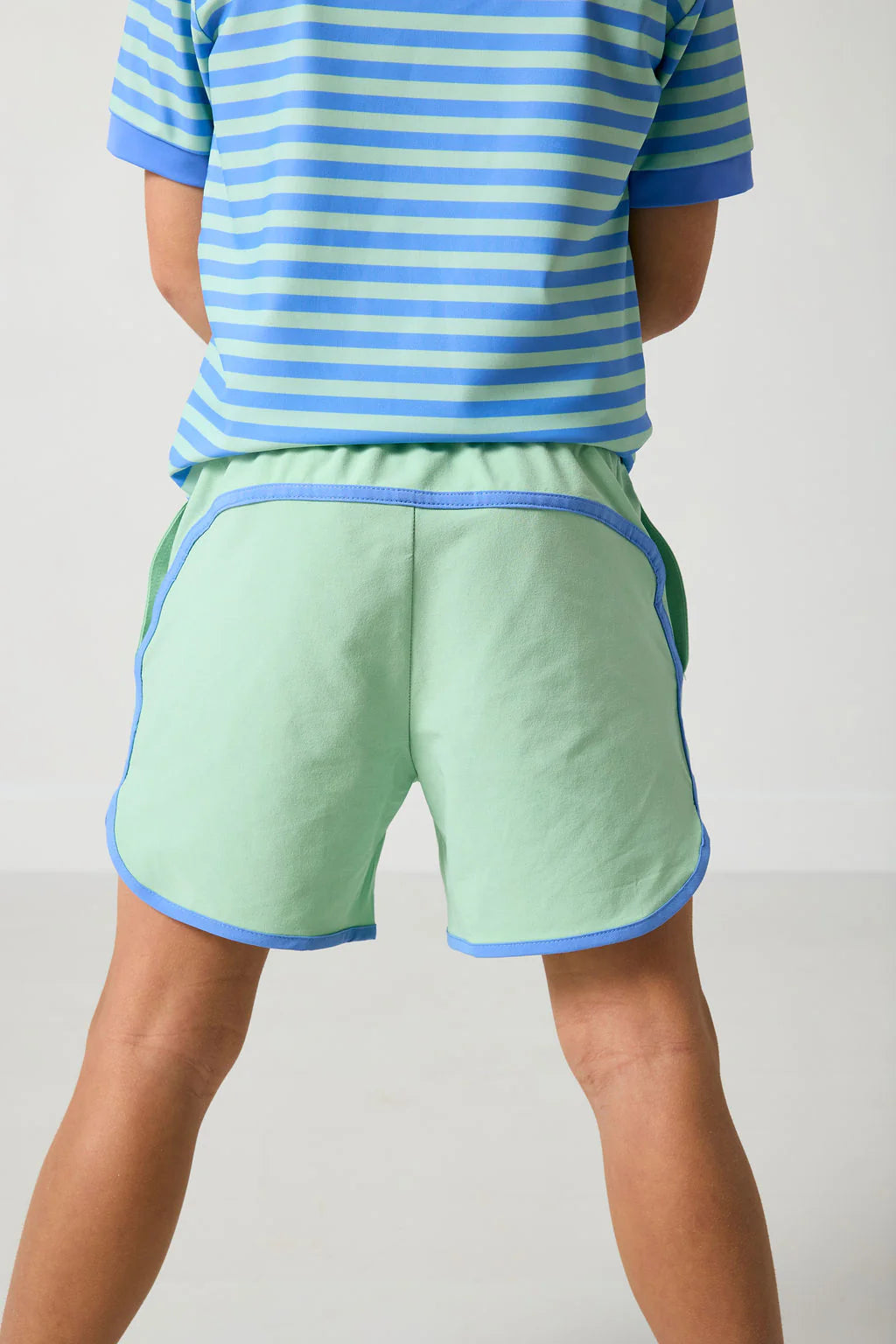 Person wearing a blue and green striped shirt and light green shorts on a plain background