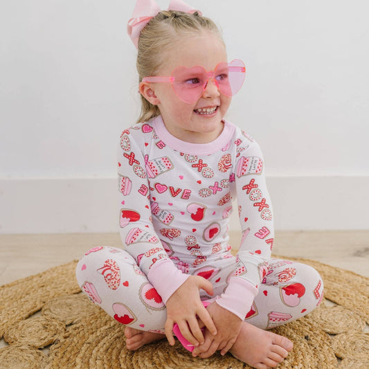 Child wearing a Valentine's Day-themed outfit with heart-shaped glasses on a beige rug.