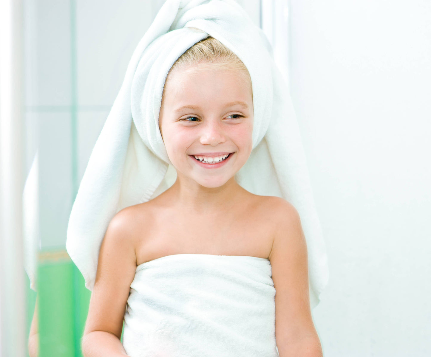 Young girl wrapped in a towel with a white towel on her head, smiling.