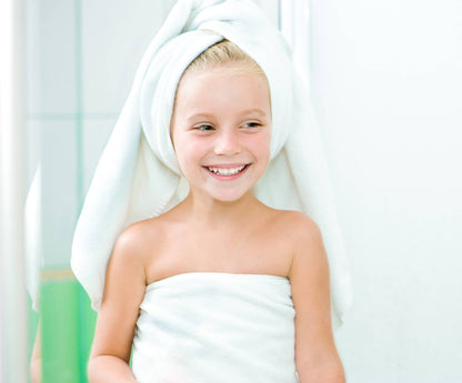 Young girl wrapped in a towel with a white towel on her head, smiling.