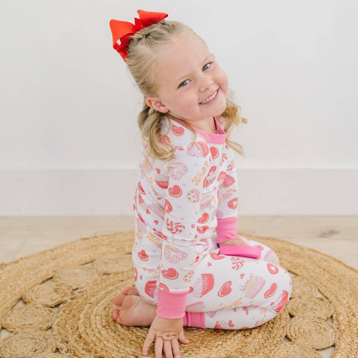 Young girl wearing a patterned onesie sitting on a woven mat.