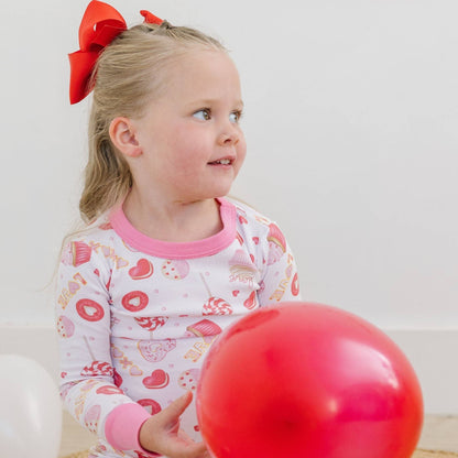 Child wearing pajamas with a red bow in hair, holding a red balloon against a white background