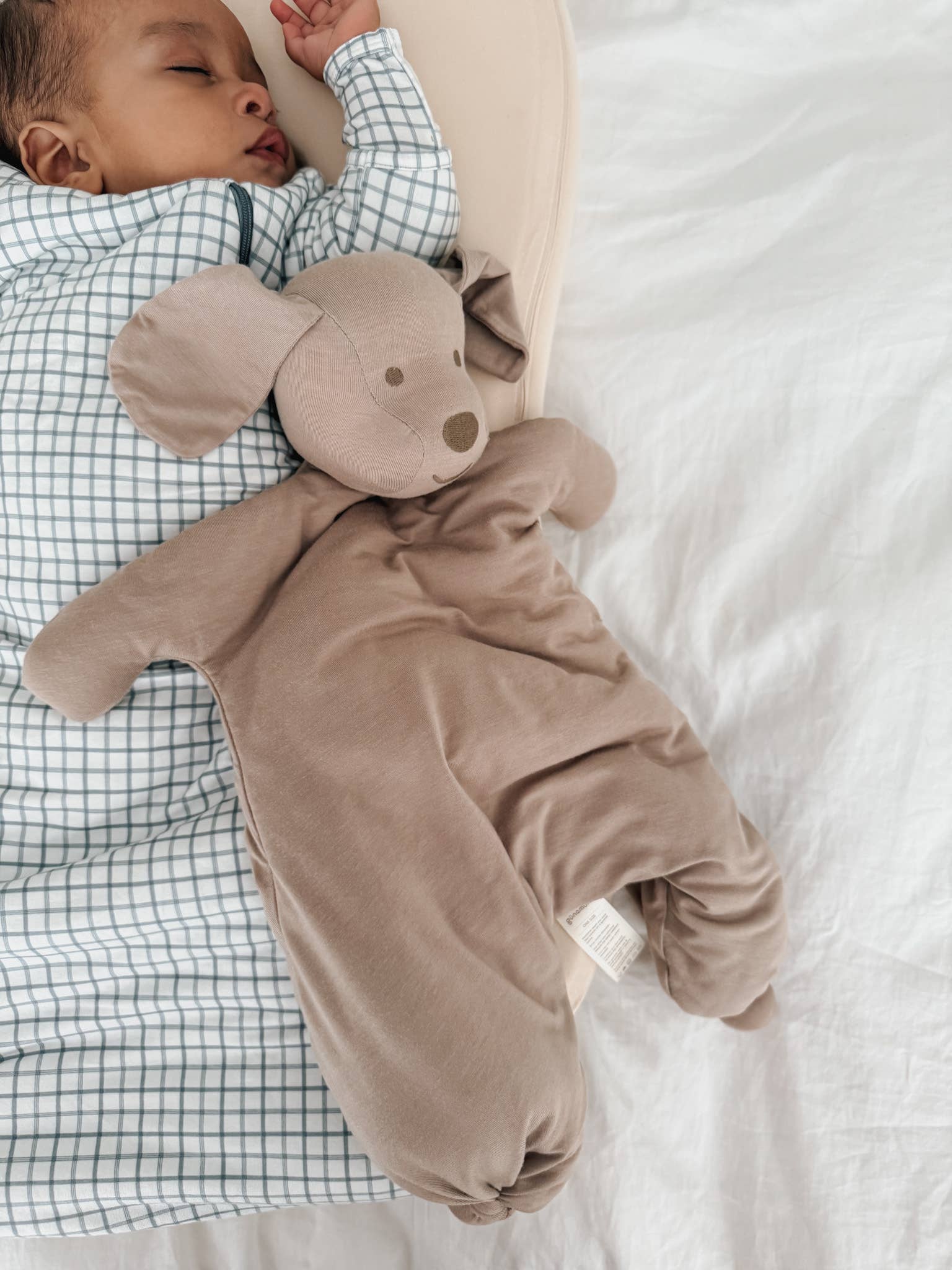 Baby in a brown onesie with a hood, lying on a white blanket.
