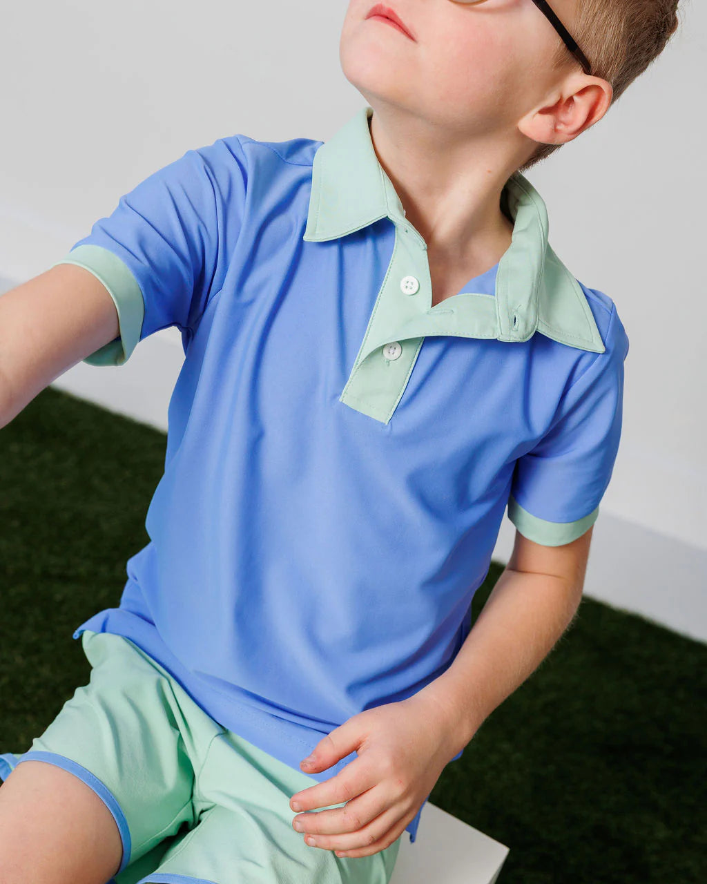 Child wearing a blue and green polo shirt and shorts set on a neutral background
