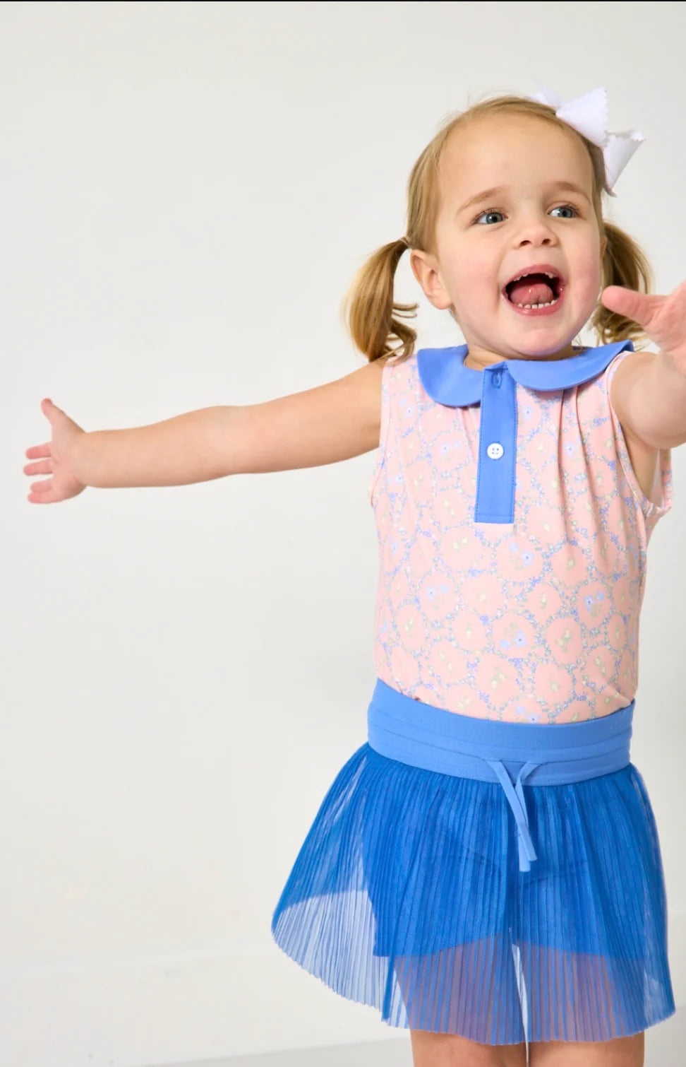 Child wearing a pink top with blue collar and blue skirt on a white background