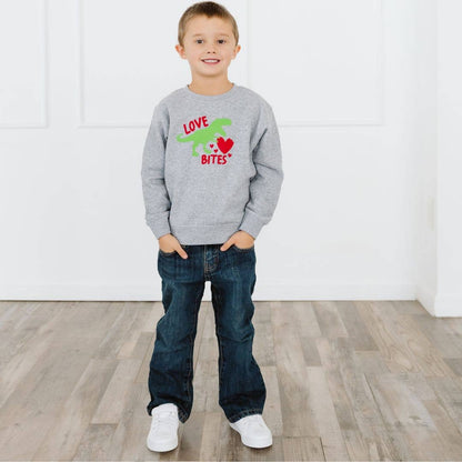 Child wearing a gray sweatshirt with a dinosaur graphic and text, standing on a wooden floor.