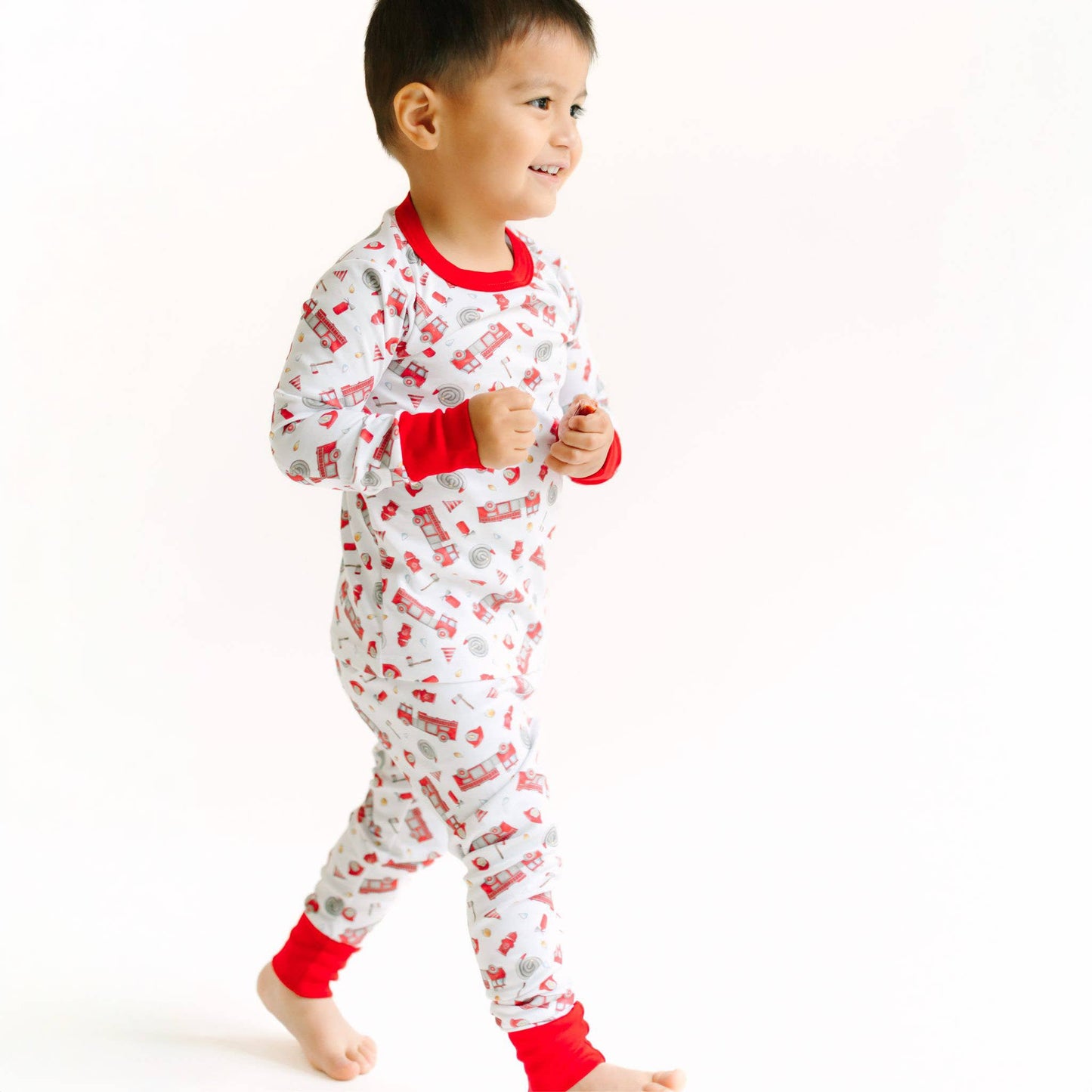 Child wearing a white onesie with red accents and fire truck pattern on a white background