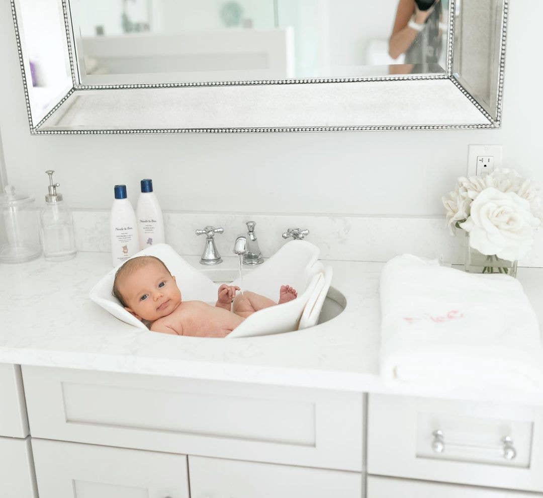 Baby in a white basin with a mirror above in a bathroom setting