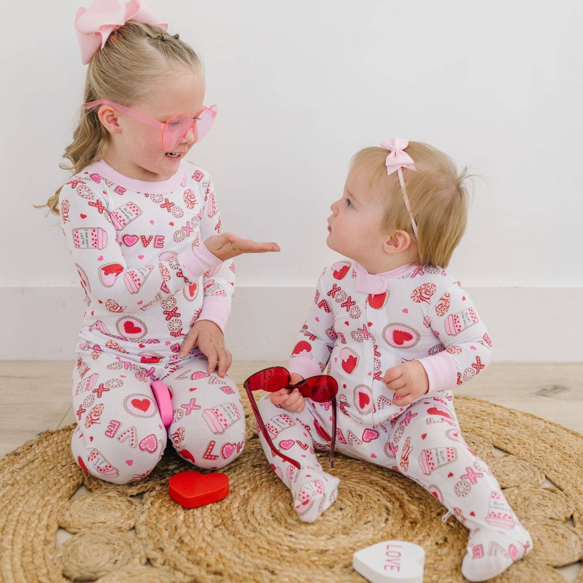 Two children in Valentine's Day pajamas sitting on a woven mat.