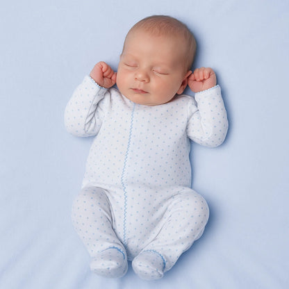Newborn baby sleeping in a white onesie with blue dots on a light blue background